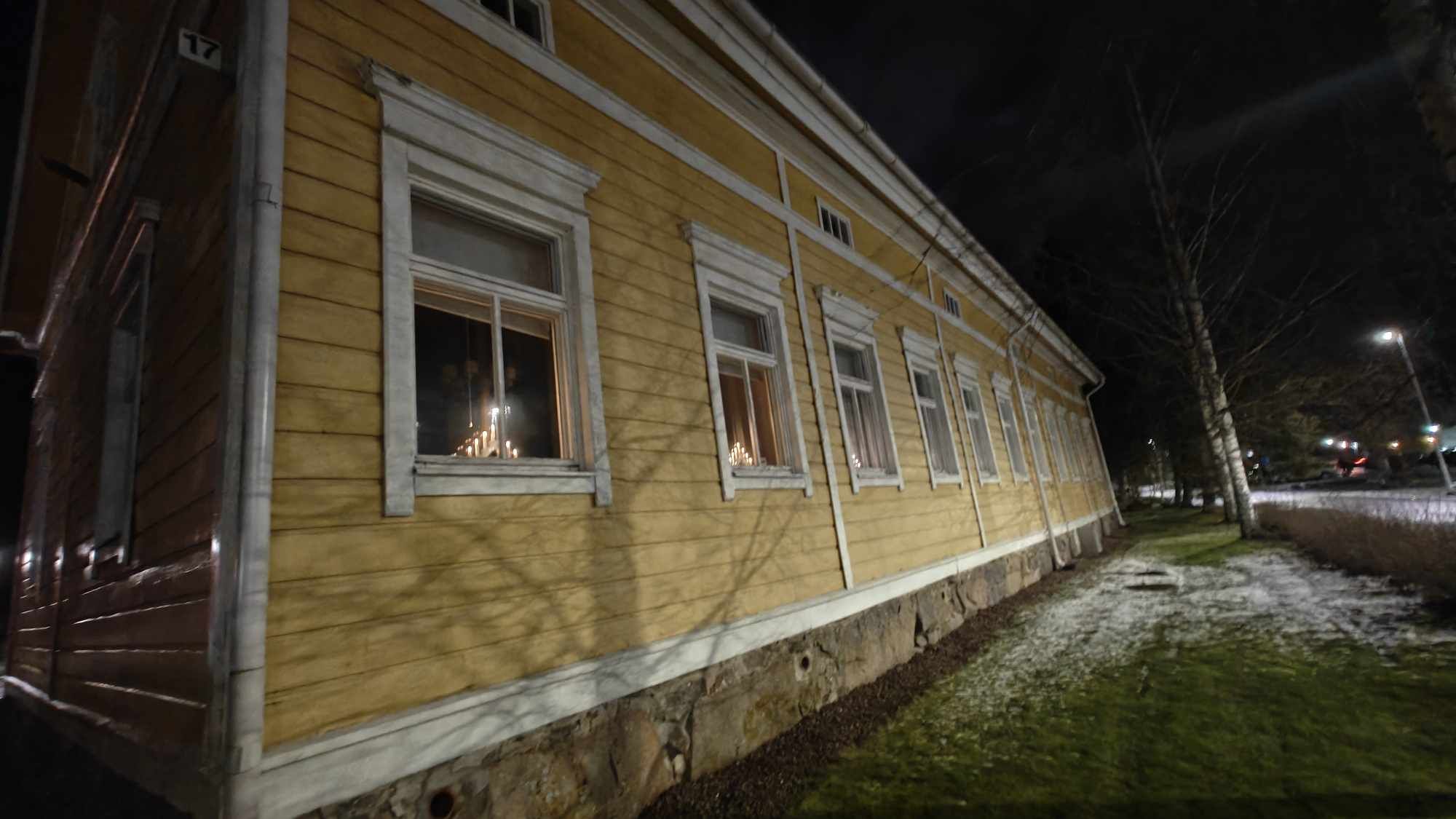 Keltaisen puisen Liedon pappilan pitkä julkisivu iltahämärässä ikkunoillaan adventtikynttilöitä.