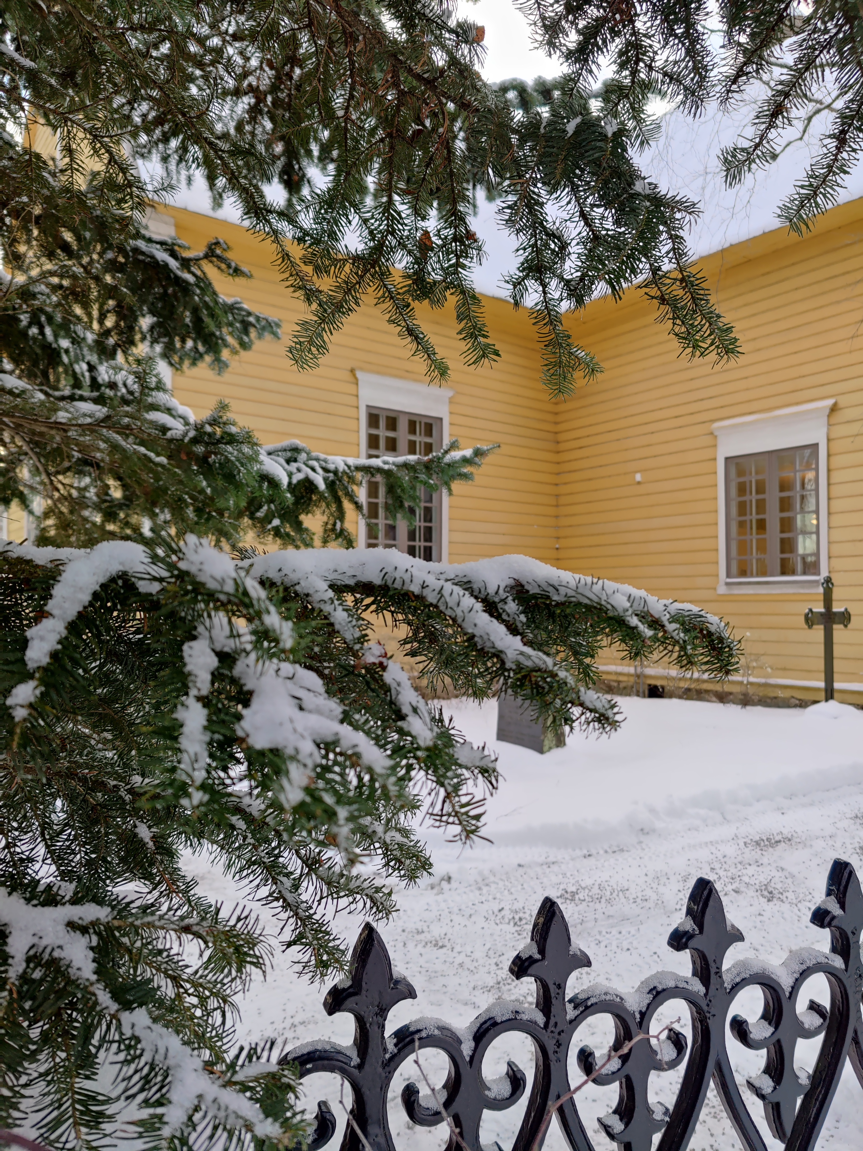 Edessä luminen kuusen oksa, taustalla Tarvasjoen kirkon seinä.