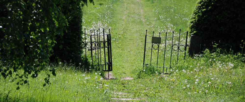 Viinmäen hautausmaalle johtava rautaportti avoinna ja edessä ja takana vihreää nurmialuetta.