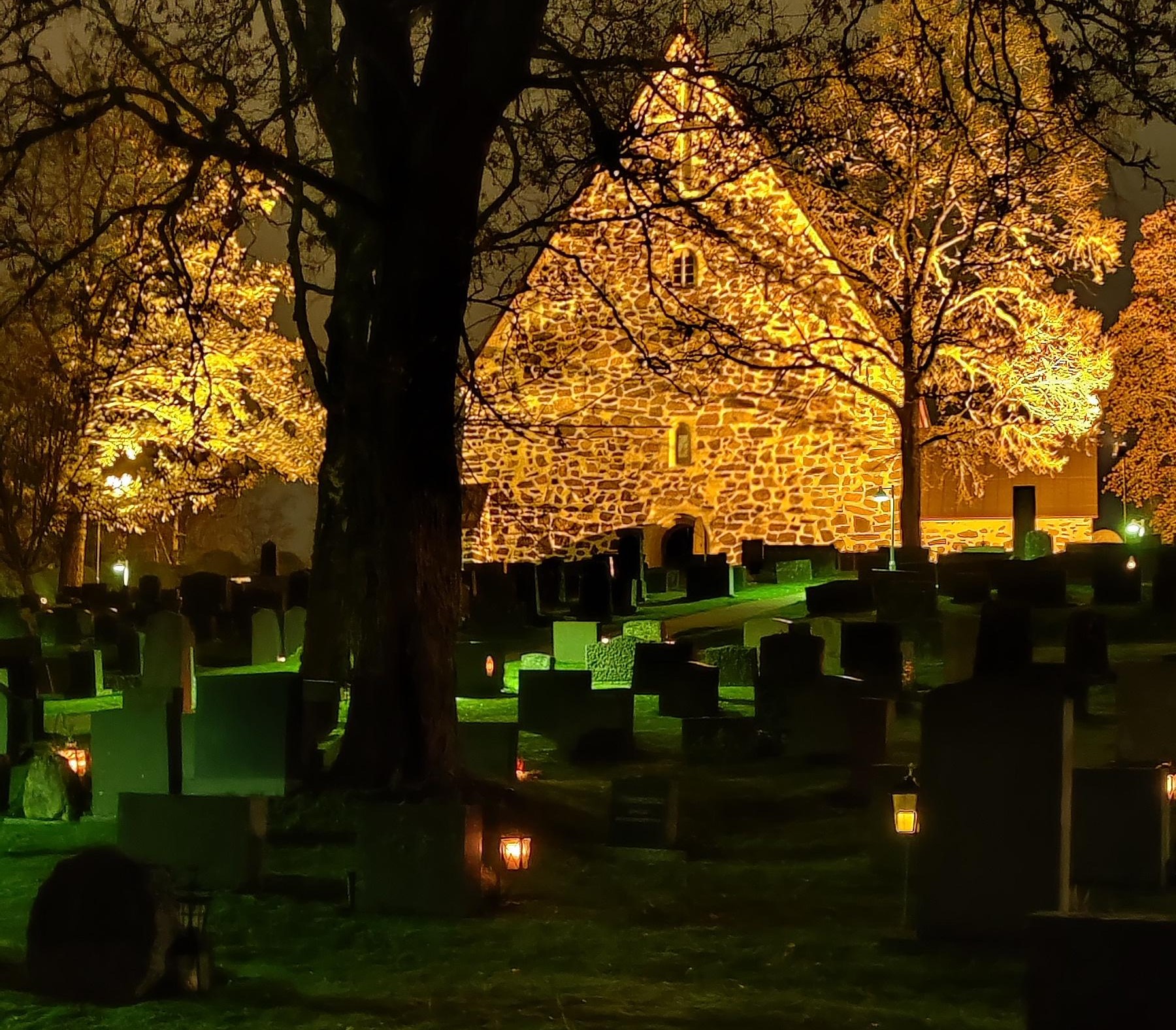 Hautoja pimeällä hautausmaalla ja Liedon kirkon länsipääty.