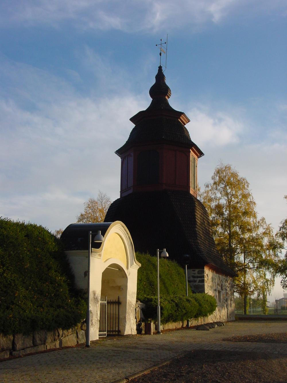 Keskiaikainen kirkon portti ja melko tummana näkyvä kellotapuli taustalla taivas.