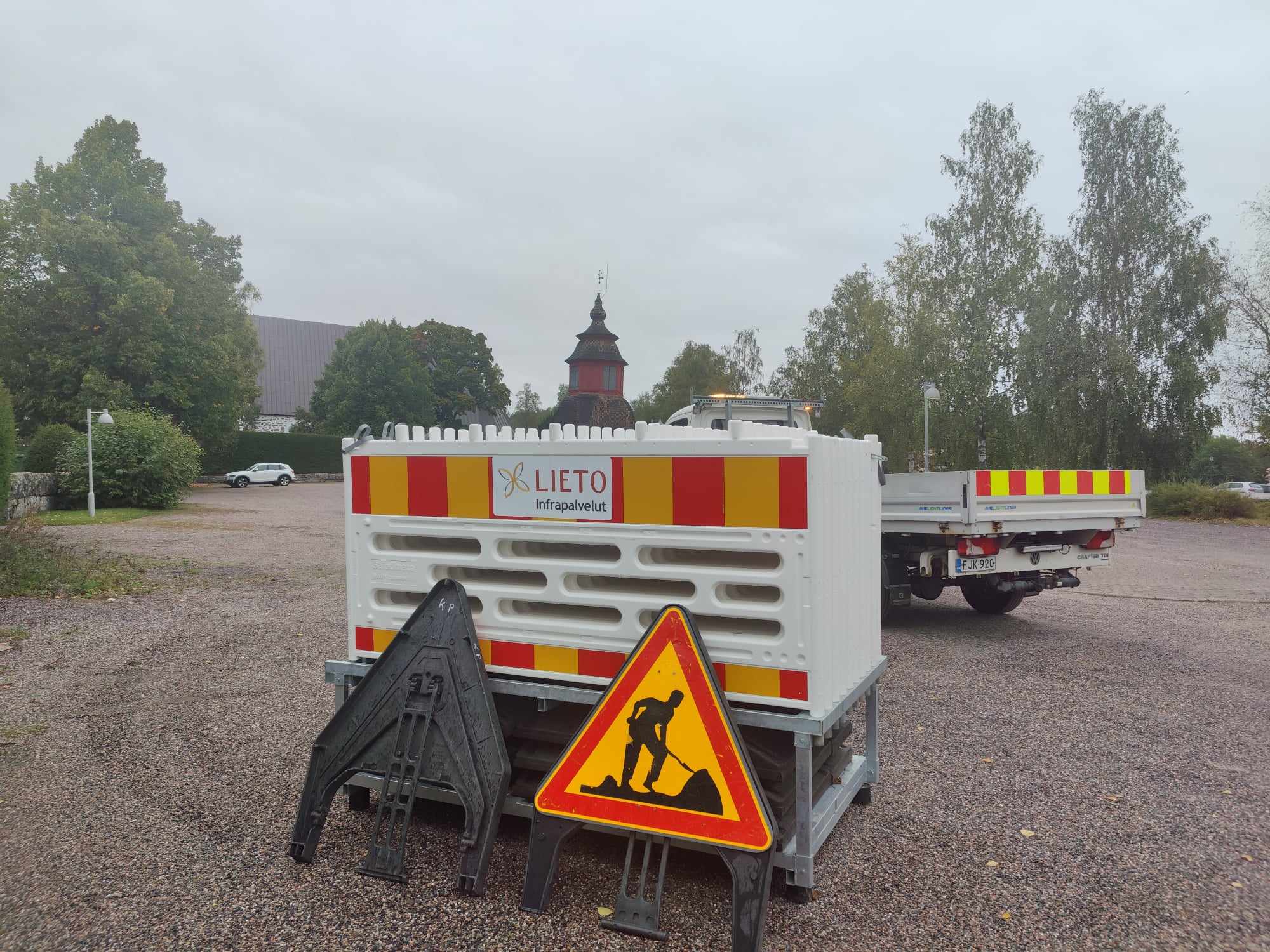 Työmaakyltti ja työmaa-aitoja Liedon kirkon edustalla pysäköintialueella.