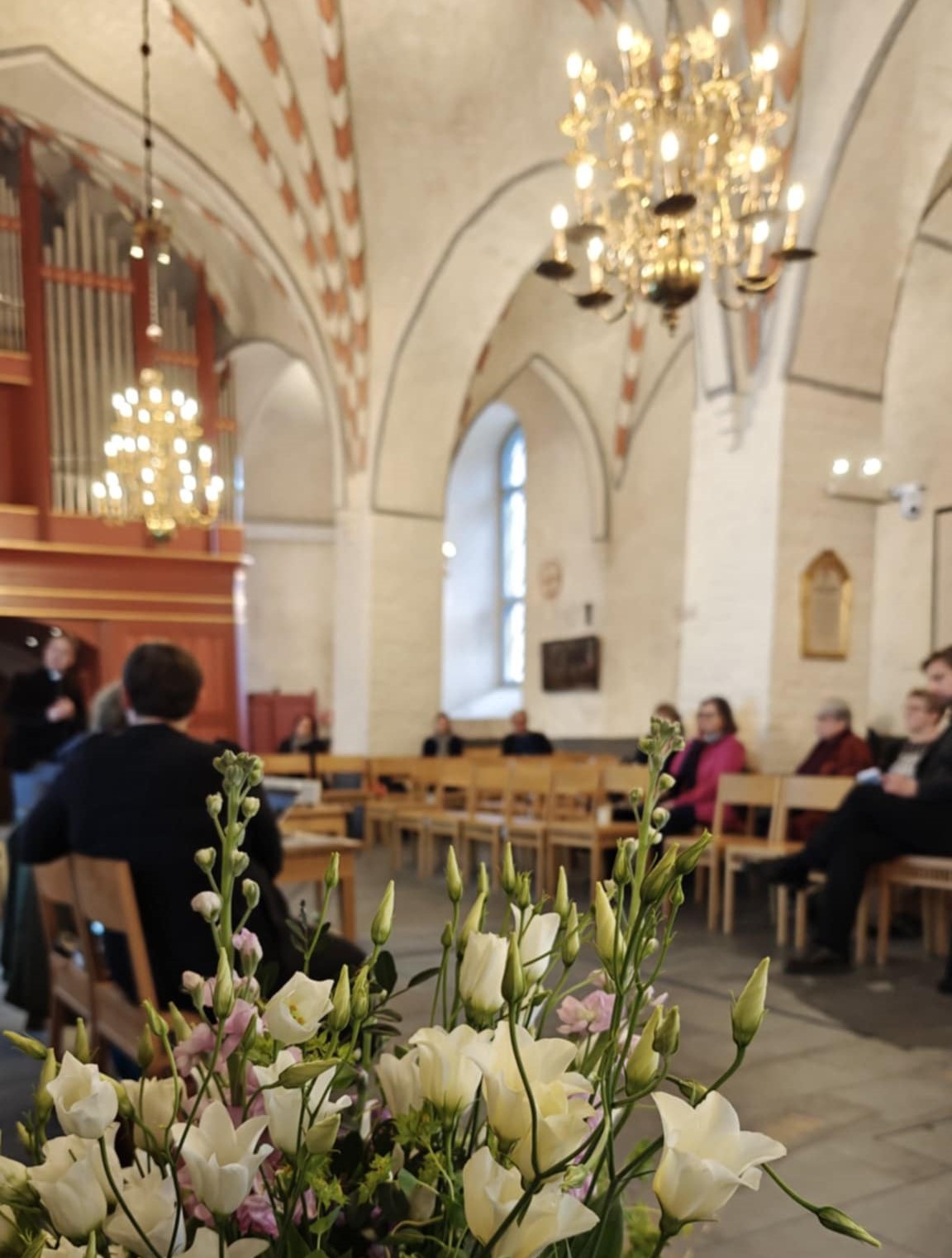 Etualalla kukkia ja taustalla väkeä kirkkosalissa.
