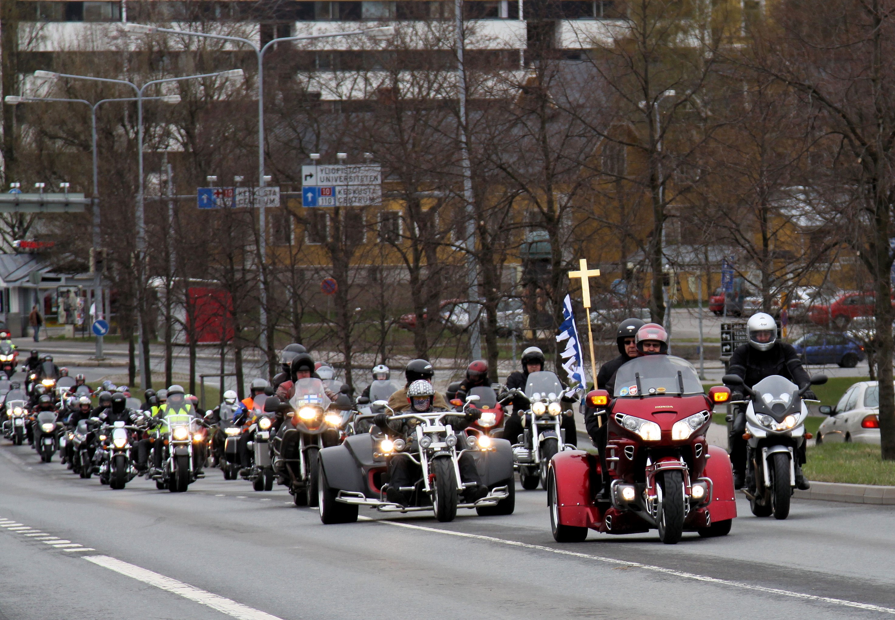 Motoristikirkon kulkue kaupungin kadulla kärjessä johtopyörä jonka kyydissä ristinkantaja risteineen.