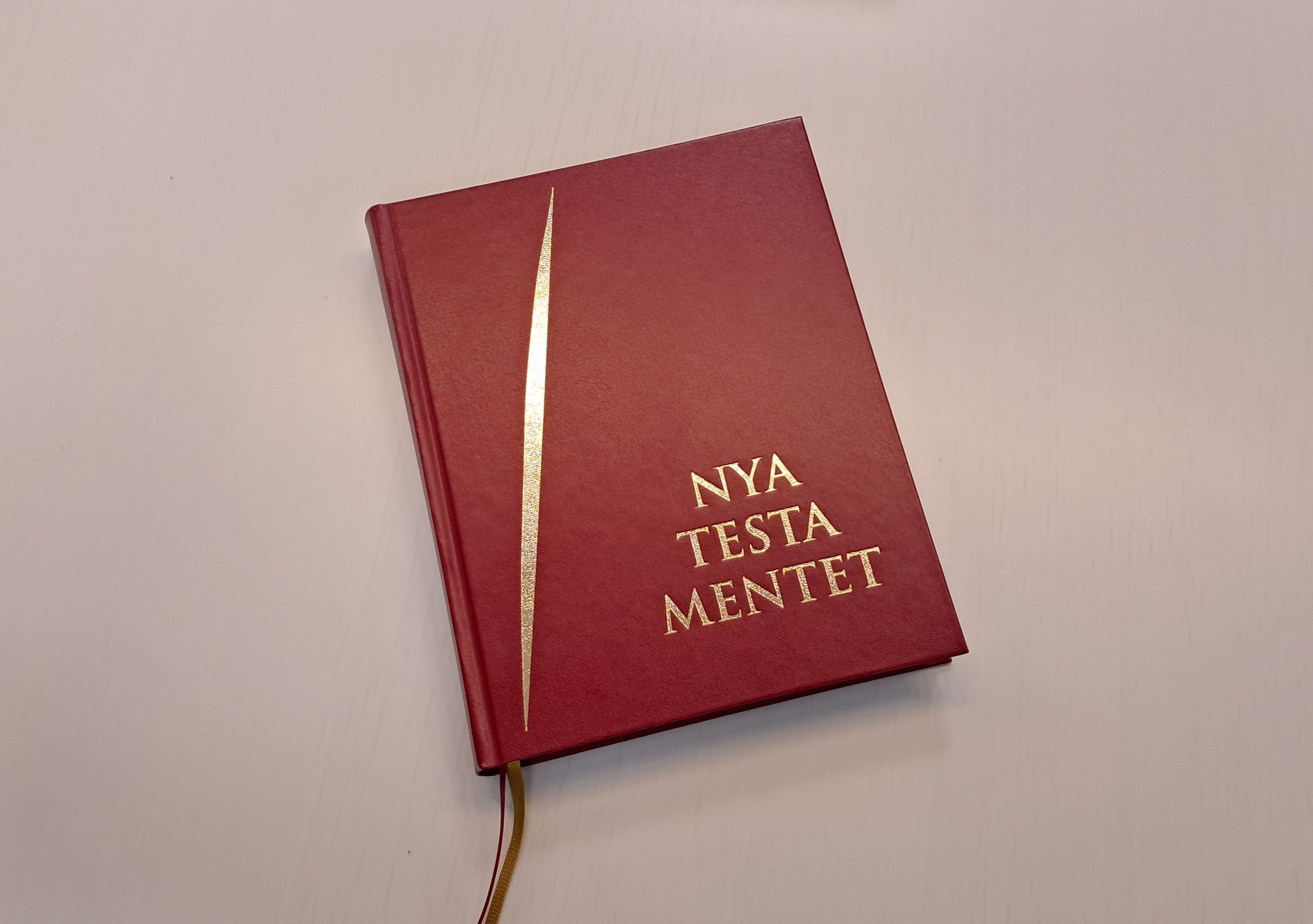 Punakantinen kirja ja kannessa teksti Nya testamentet.