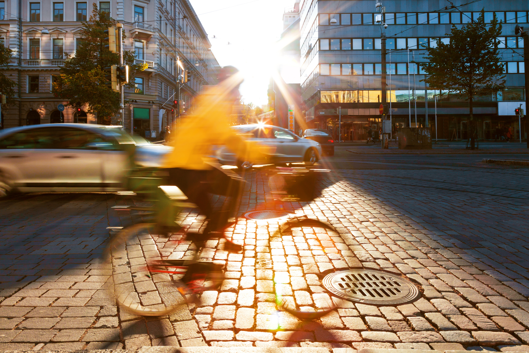Kuvituskuvassa kaupungin keskustaa, autoliikennettä ja etualalla epätarkasti viitteellisesti näkyvä pyöräil...