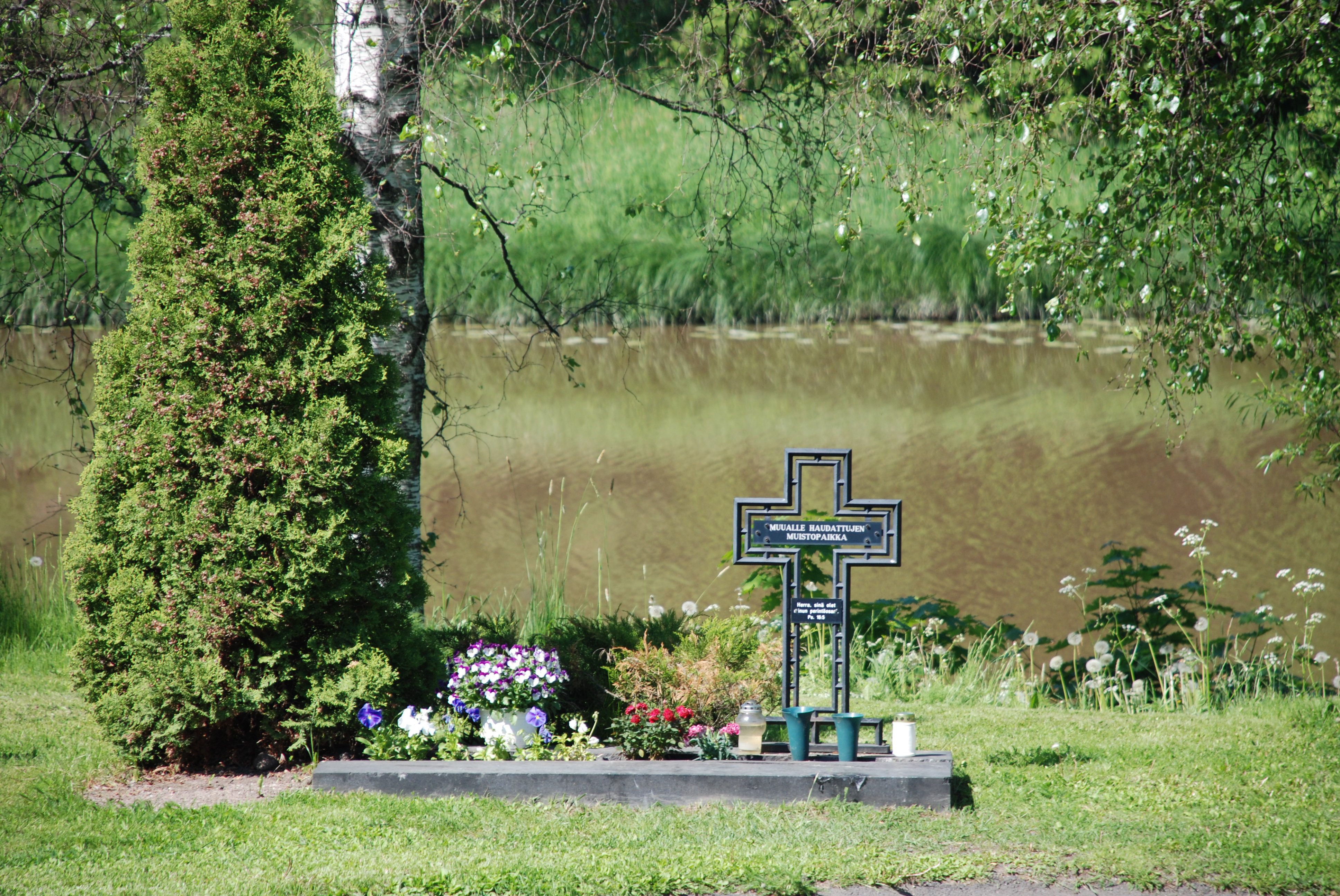 Muualle haudattujen muistopaikka kesällä joen varrella.