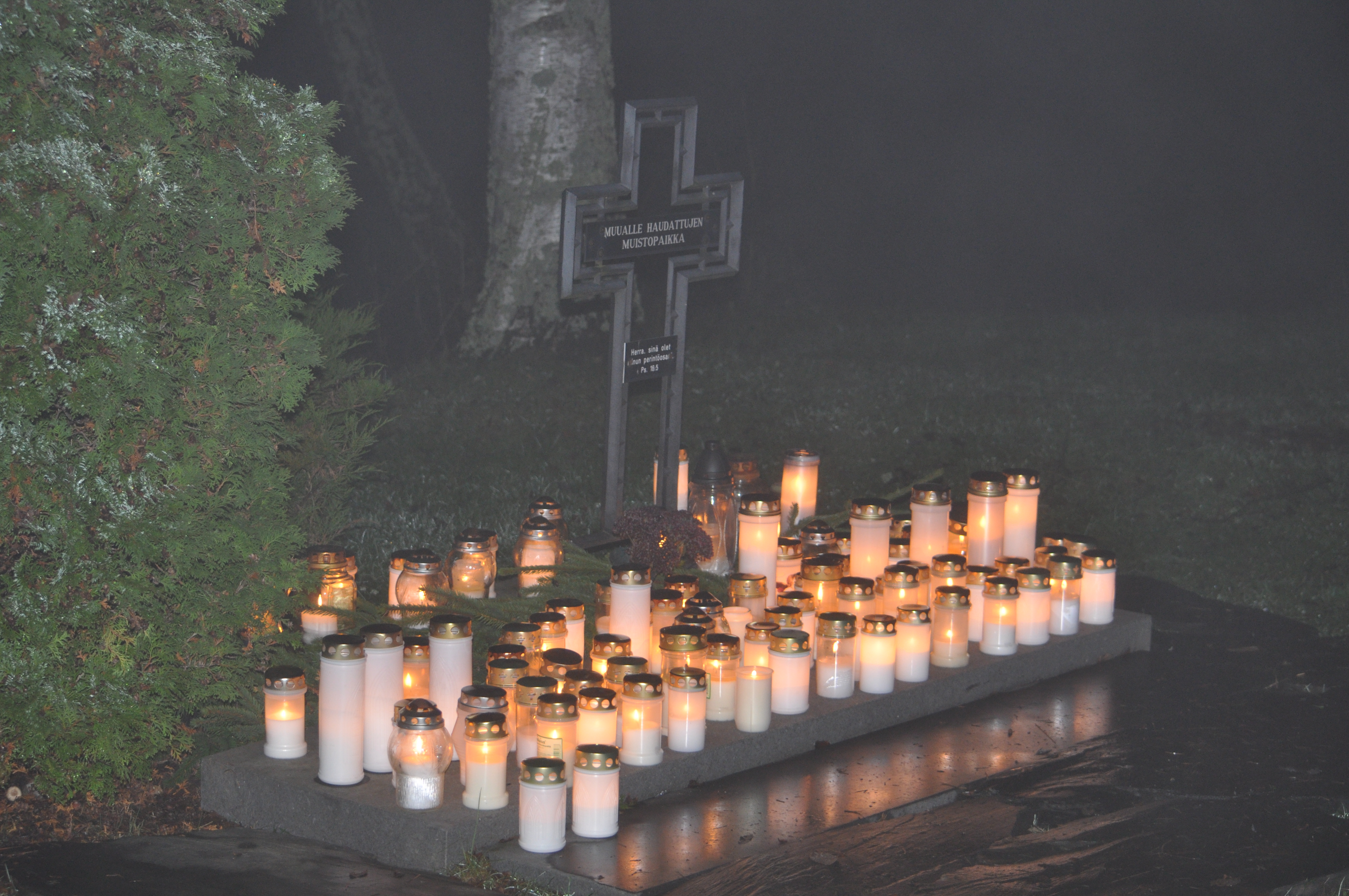 Pyhäinpäivän hämärässä kynttiläpaljous muualle haudattujen muistopaikalla.