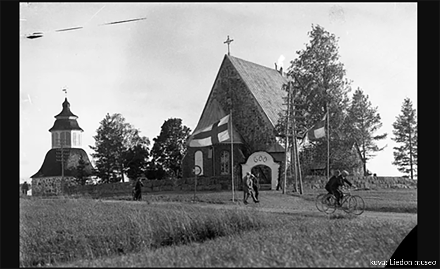 Mustavalkoisessa vanhassa kuvassa papinportin takana kirkko, vasemalla näkyy kellotapuli ja tiellä edustalla kävelijöitä ja  pyöräilijöitä sekä lippu salossa kirkon 600-vuotisjuhlassa. 