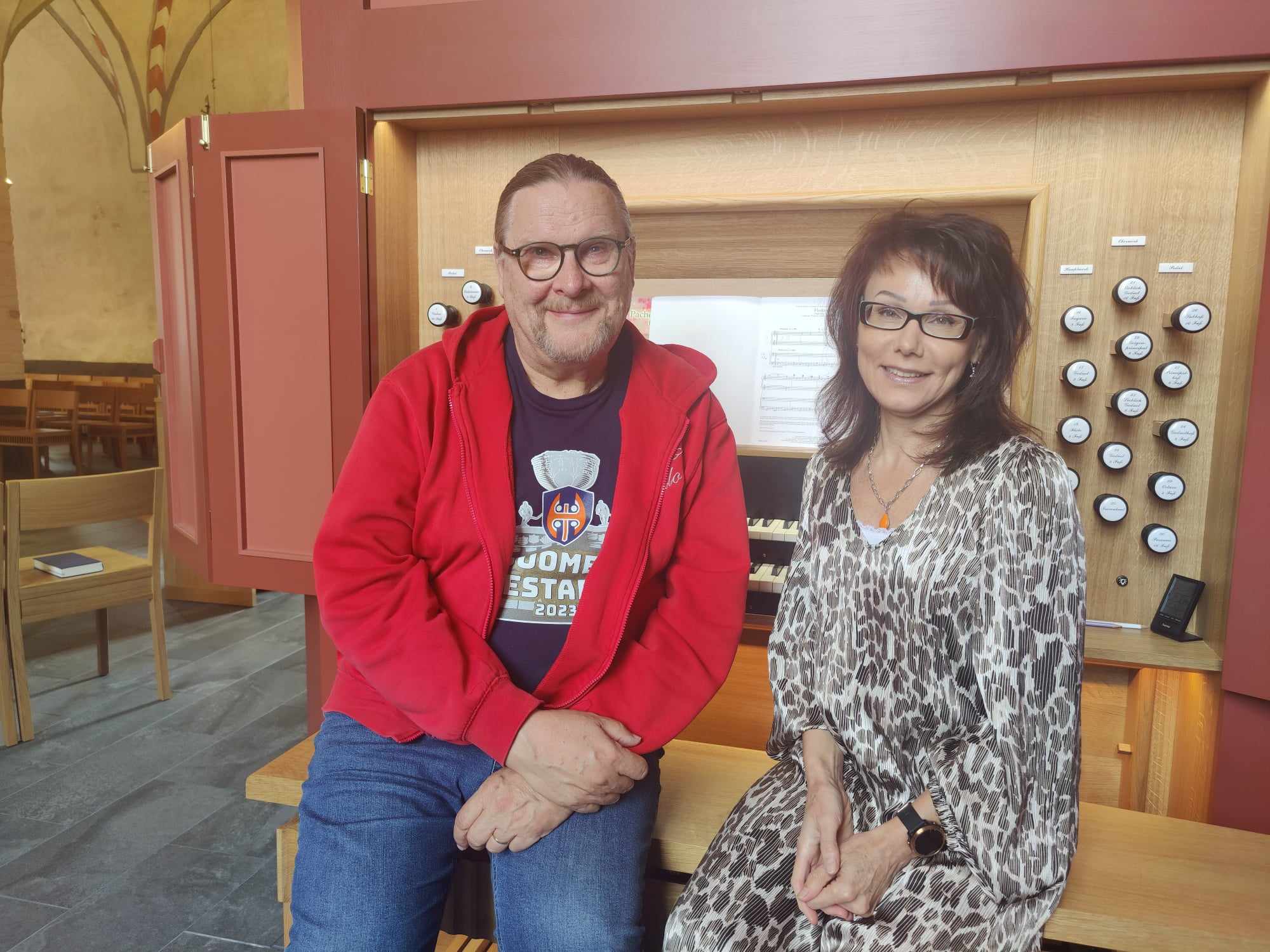 Hannu Ilola ja Svetlana istuvat Liedon kirkon urkujen edustalla kasvot kameraan päin selin soittopöytään.