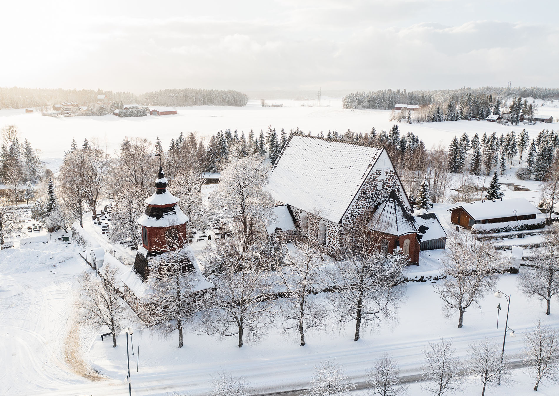 Liedon kirkko, kellotapuli, hautausmaata ja muuta kirkon ympäristöä talvisessa miljöössä ilmasta kuvattuna.