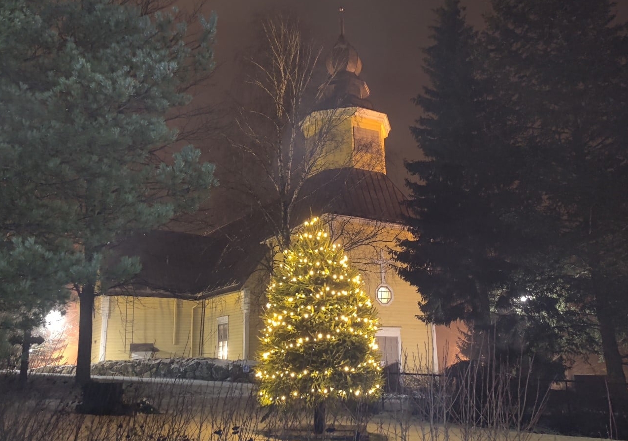 Tarvasjoen kirkko  joulun alla hämärään aikaan ja edessä jouluvaloin valaistu kuusi.