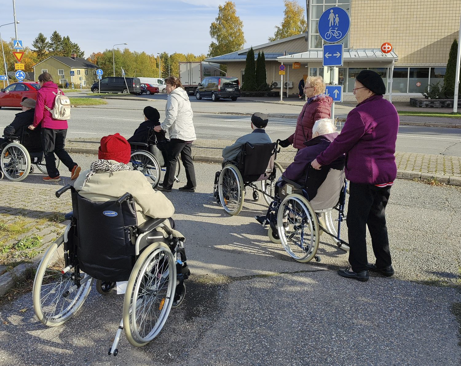 Vapaaehtoisia ulkoiluavustajia ja pyörätuoleissa ulkoilevia Auran keskustassa.