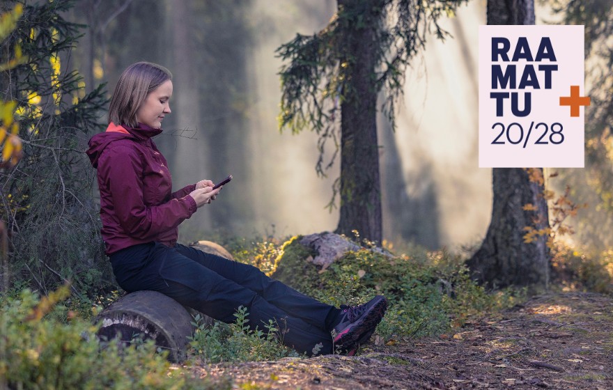 Nainen istuu metsässä puunrungon päällä ja katsoo kännykkä. Kuvassa lukee Raamattu 20/28 ja risti.