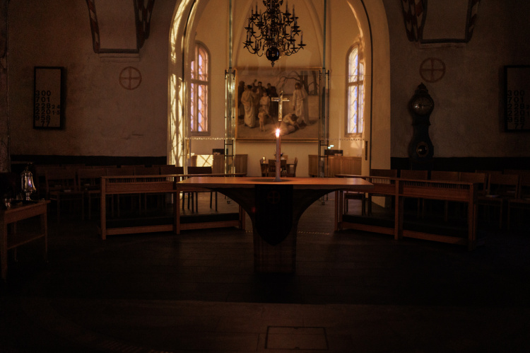 Hämärässä Liedon kirkossa alttarilla yksi kynttilä. 