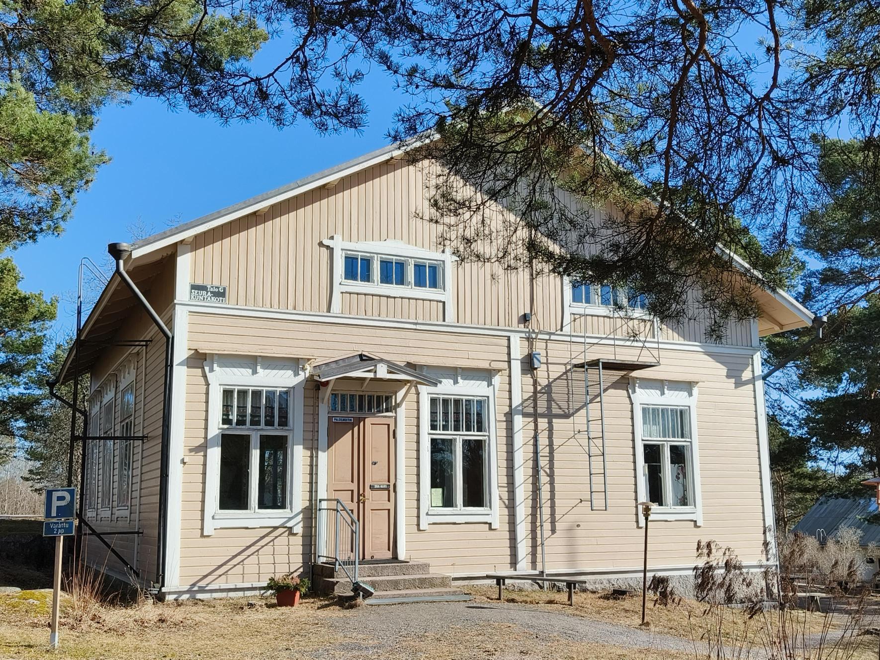 Vanha puutalo aurinkoisessa mutta kevään koruttomassa maisemassa. 