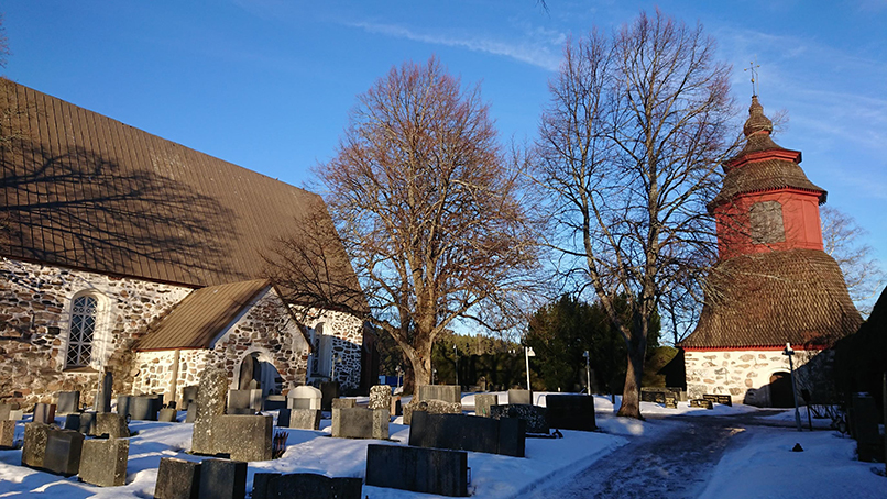 Liedon kirkko ja kellotapuli kevättalvella hautausmaalta kuvattuna.  
