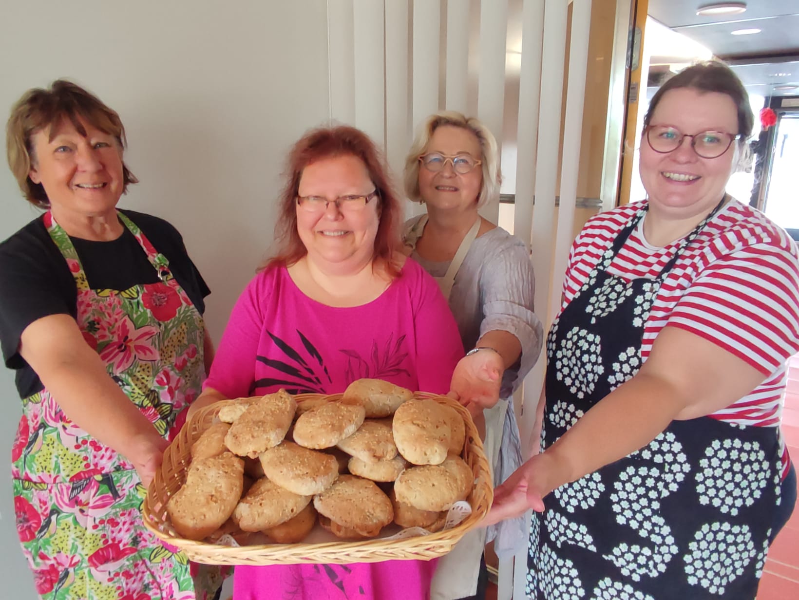 Naurava joukko leipomistalkoisiin osallistuneita ja yhdellä käsissään tarjotin täynnä valmiita sämpylöitä.