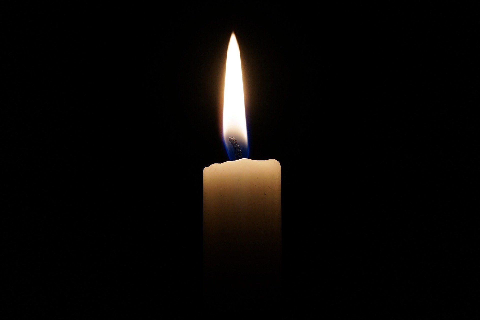 Kynttilänliekki sekä hiukan vaaleaa kynttilää näkyvissä mustaa taustaa vasten. 