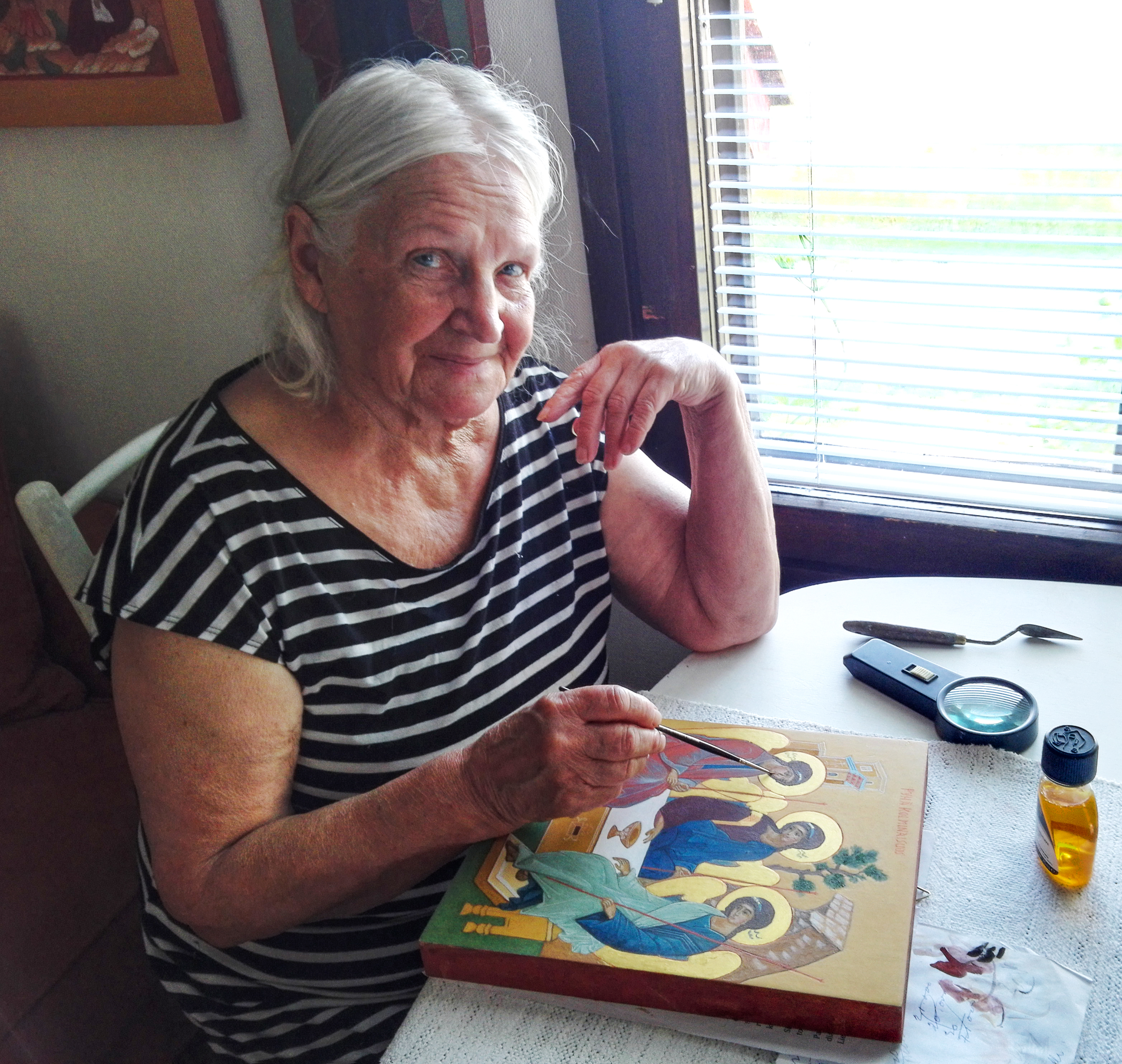Margit Vainio maalaamassa ikonia pöydän ääressä.