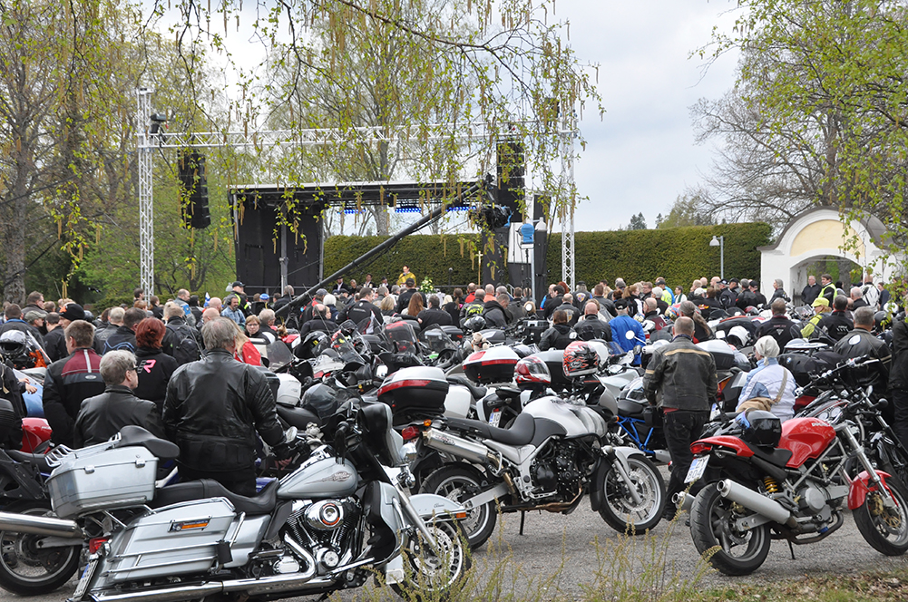 Moottoripyöriä ja ihmisiä Liedon kirkon pysäköintialueella ulkolavan edustalla keväällä 2019 motoristikirko...