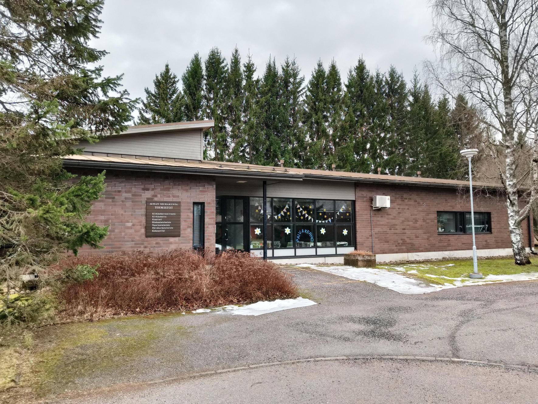 Yksikerroksinen tiilirakennus vähälumisessa kevättalven maisemassa.