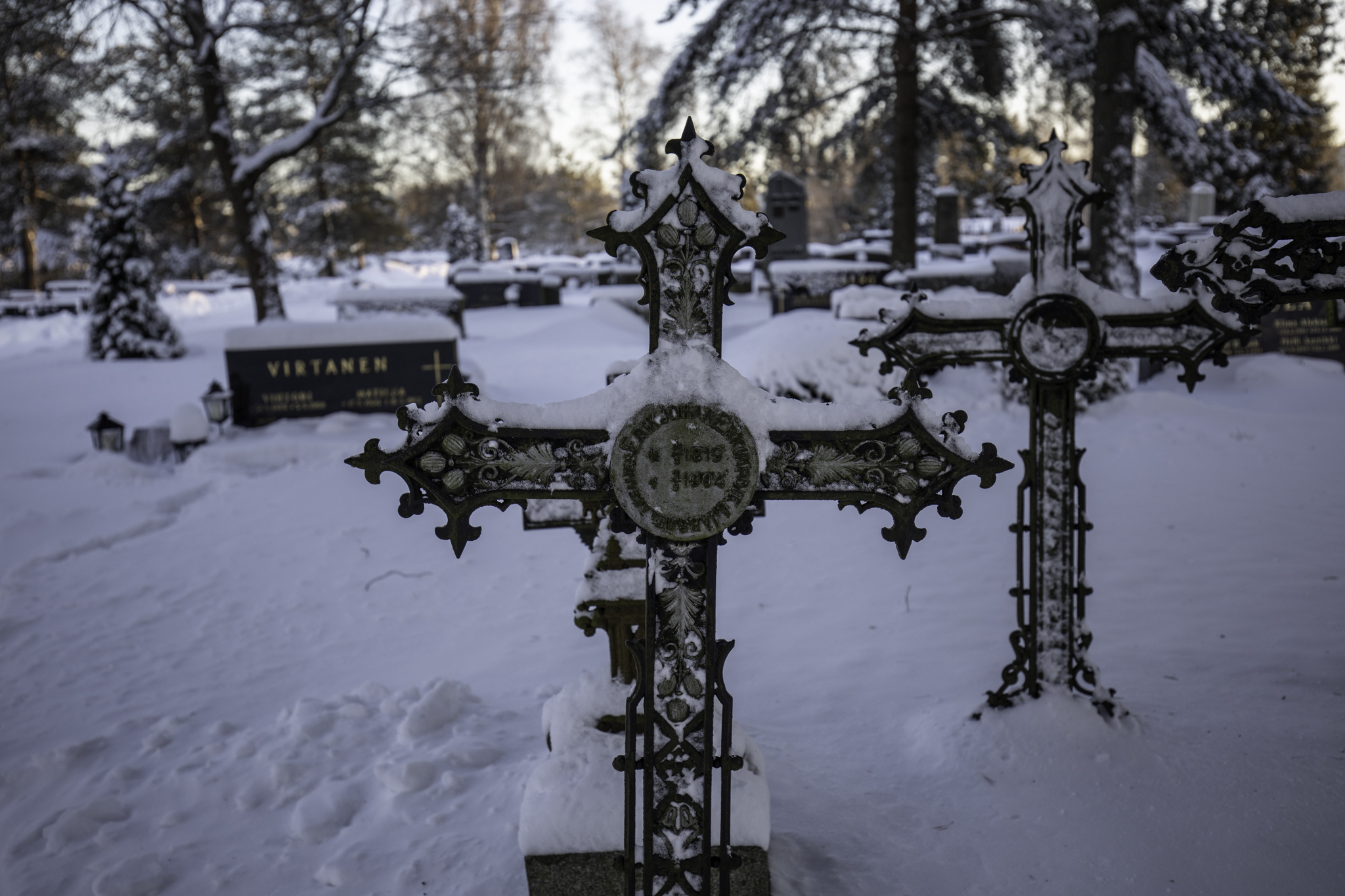 Koristeellinen rautainen hautaristi 1900-luvun alusta talvisella hautausmaalla.